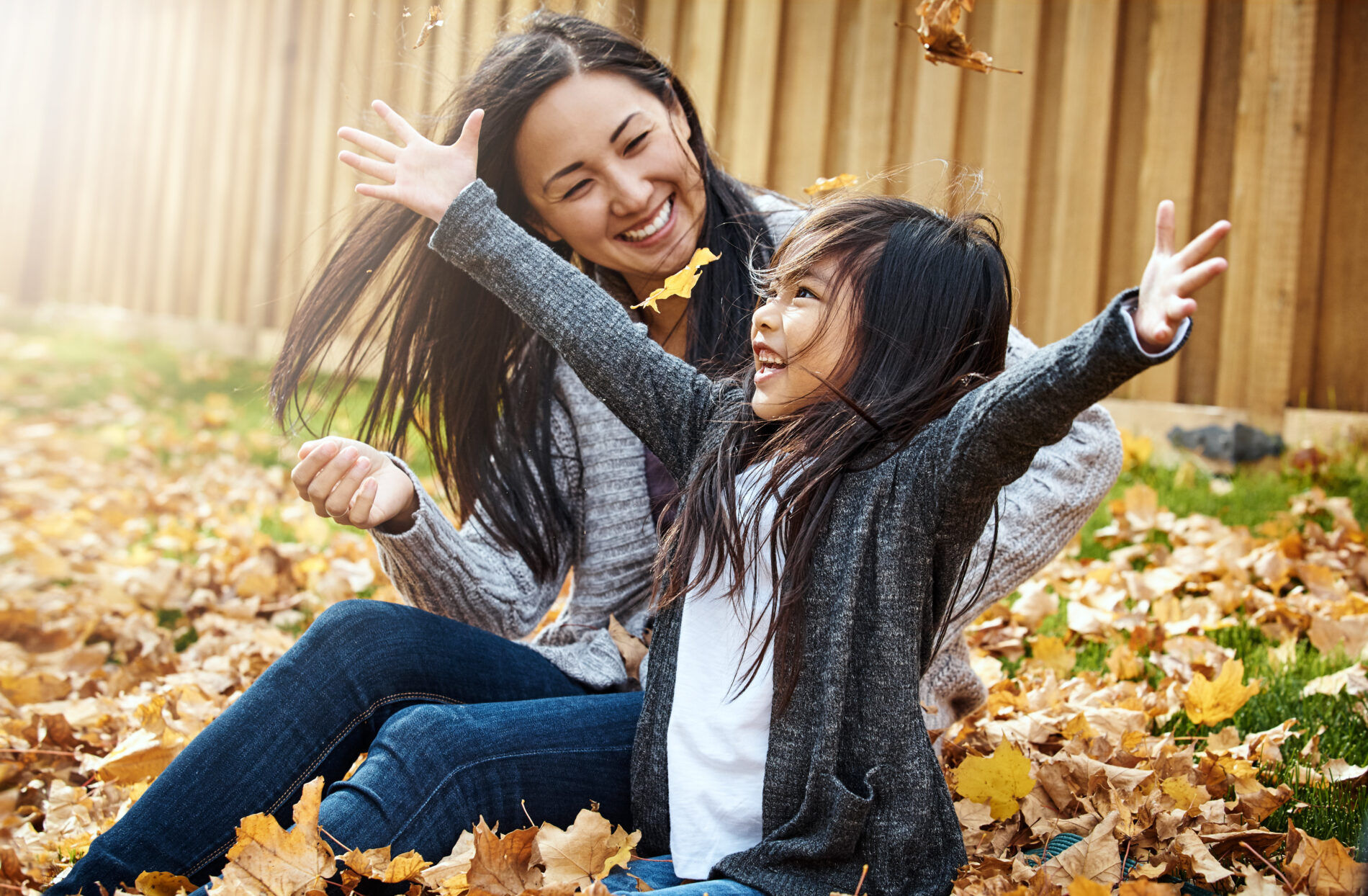 Autumn, mother and daughter leaf throwing in garden of home together for bonding or love. Asian family, fall or joy with single parent woman and girl child having fun in backyard for wellness.